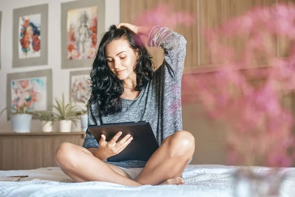 Jovem mulher atraente sorrindo conteúdo, feliz e lendo em casa tablet. Fotografia De Stock