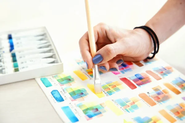 Die Wahl der Farbe für die Malerei auf Papier mit Aquarellfarben mit weiblicher Hand halten Pinsel auf Farbpalette Hintergrund. lizenzfreie Stockfotos