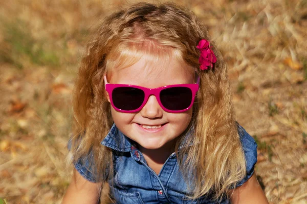 Little girl sitting in pink sunglasses looks and smiles — Stock Photo, Image