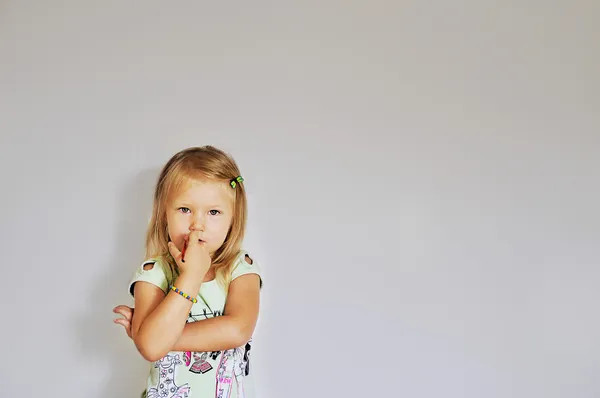 Little girl stands by the wall and holding a brush in his mouth — Stock Photo, Image