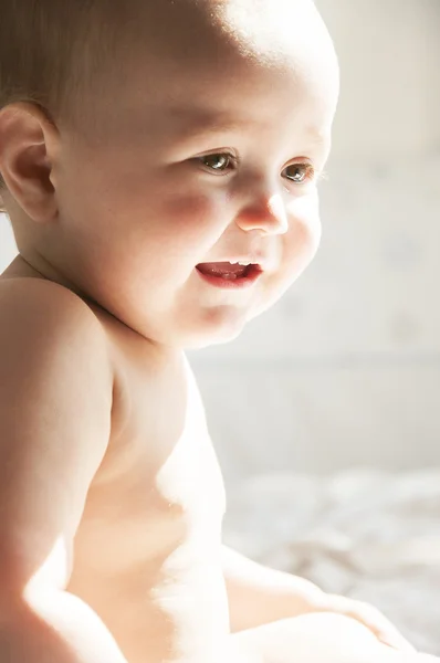 Sorrindo bebê sentado na cama e olha — Fotografia de Stock