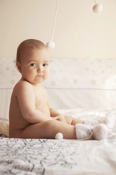 ニットの靴下でベッドの上に座っている若い赤ちゃん ロイヤリティフリーのストック写真