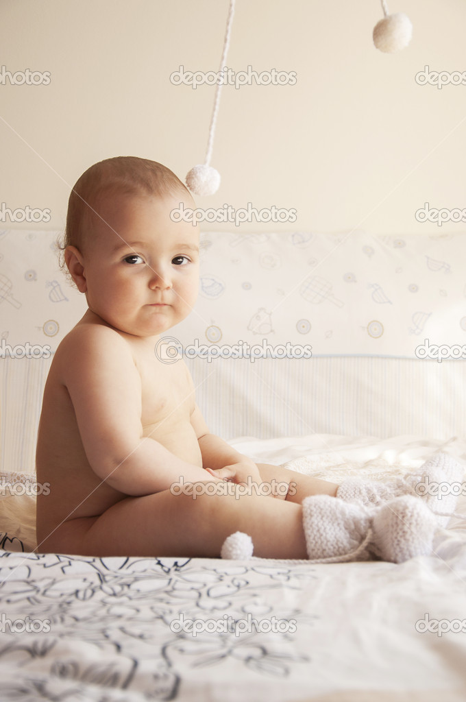 Young baby sits on a bed in knitted socks