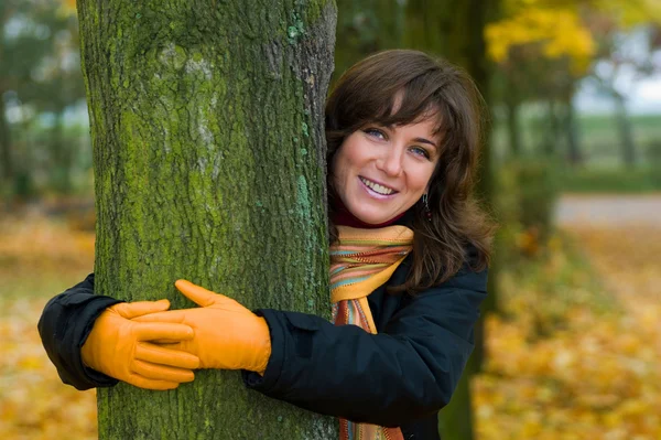 Frumoasă femeie romantică care îmbrățișează un copac - fundal de frunze de toamnă aurie — Fotografie, imagine de stoc