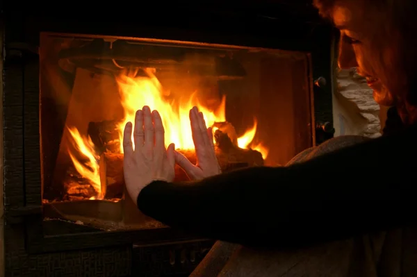 Woman warms up by the fire / fireplace — Stock Photo, Image