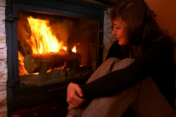 Vrouw opwarmt door het vuur / open haard — Stockfoto