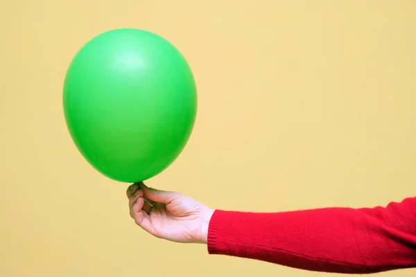 Green balloon in hand on a yellow background — Stock Photo, Image
