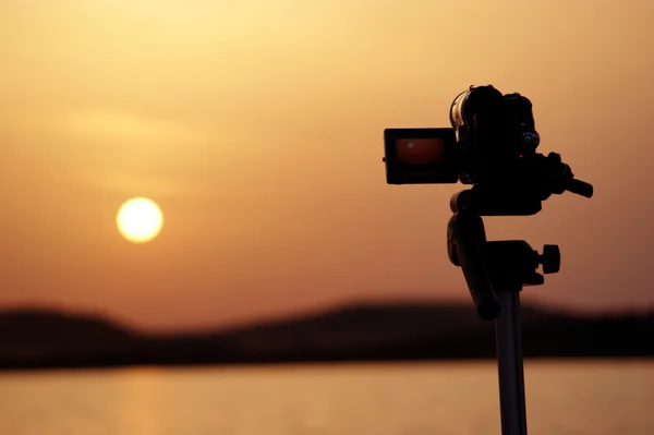 Silhouette of a camera on the tripod taking videos of a sunset — Stock Photo, Image