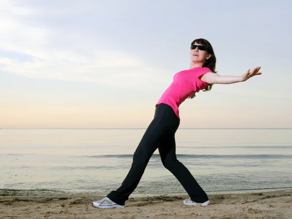 Vrouw uitoefenen op het strand bij zonsondergang in zonnebril, tinten — Stockfoto