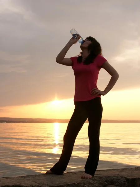 Bela jovem esportiva bebendo na frente de um pôr do sol . — Fotografia de Stock