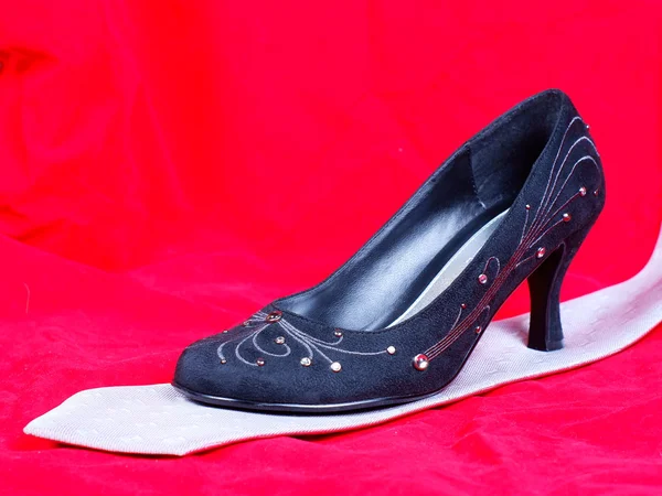 Zwarte vrouwelijke schoenen en stropdas op rode achtergrond — Stockfoto