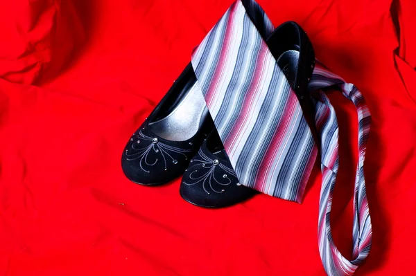 Черные женские туфли и галстук на красном фоне — стоковое фото