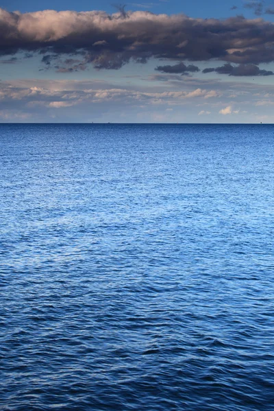 Облачно-голубое небо уходит к горизонту голубой поверхности моря — стоковое фото