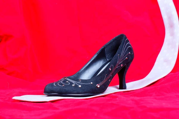 Zwarte vrouwelijke schoenen en stropdas op rode achtergrond — Stockfoto