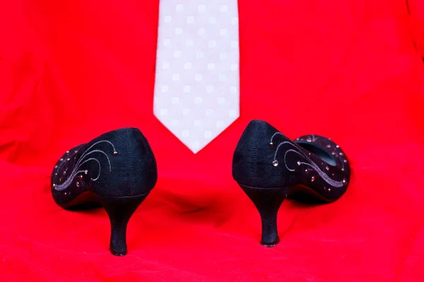Siyah kadın ayakkabı ve kravat kırmızı zemin üzerine — Stok fotoğraf