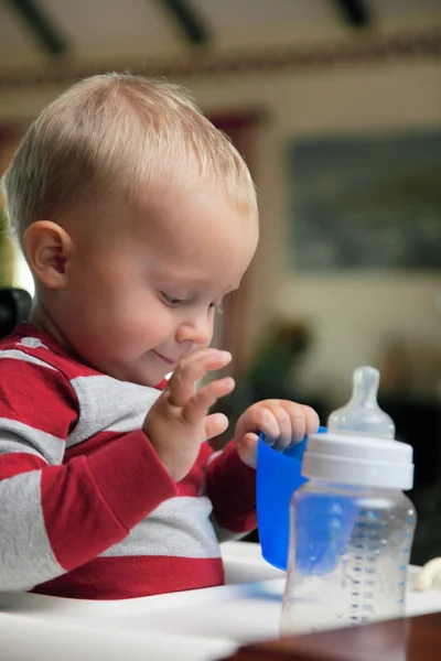 Baby boy spelen met fles en mok binnen — Stockfoto