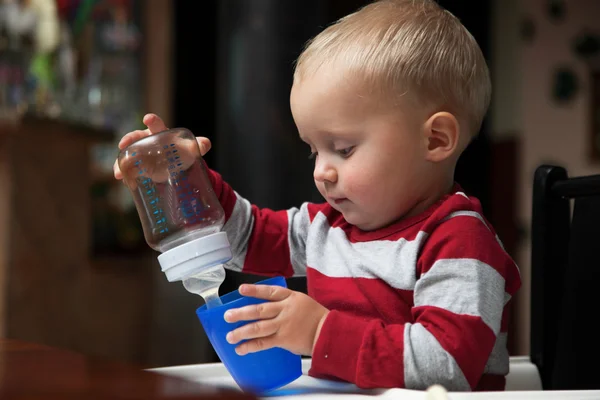 Menino brincando com garrafa e caneca interior — Fotografia de Stock