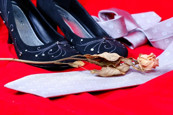 Black female shoes, rose and necktie on red background — Stock Photo, Image