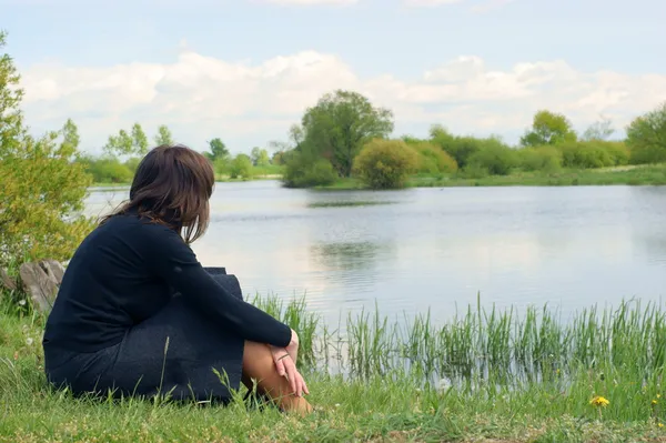 A woman sits alone and looks out across the river. — Stock Photo, Image