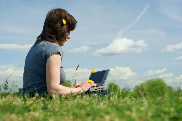 Frau tippt draußen auf einer Wiese auf einem Laptop — Stockfoto