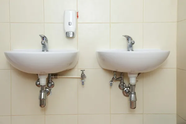 Две белые раковины и краны в общественном туалете — стоковое фото