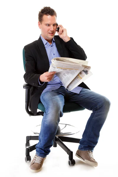 Young businessman reads newspaper while phoning — Stock Photo, Image