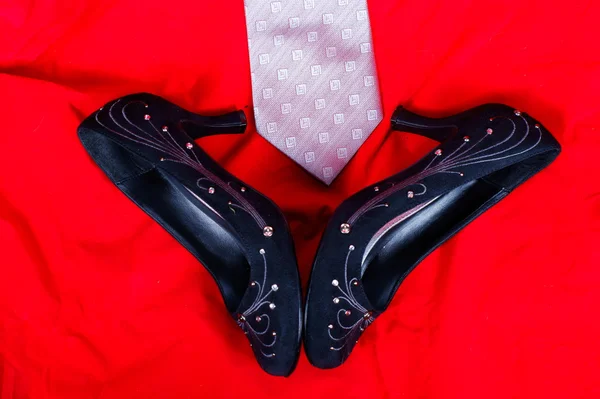 Черные женские туфли и галстук на красном фоне — стоковое фото