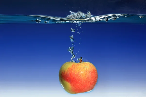 Apple in the water splash over blue background — Stock Photo, Image