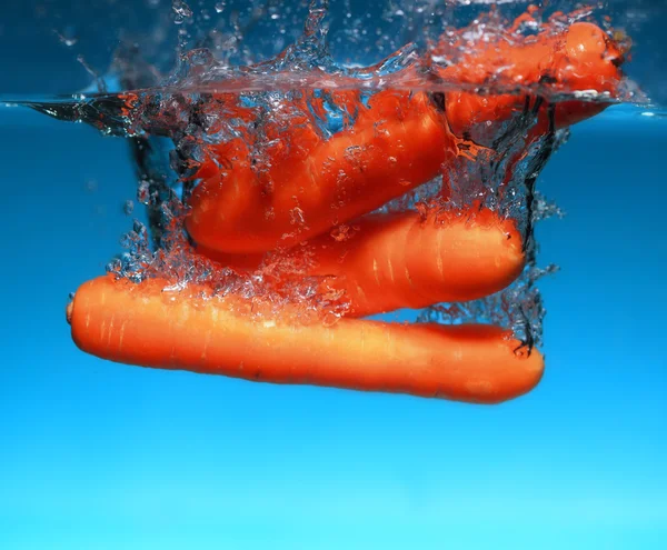 Zanahoria en el agua salpica sobre azul —  Fotos de Stock