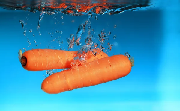 Carota nell'acqua spruzzata sopra il blu — Foto Stock