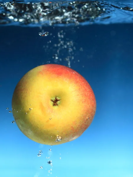 Gele appel in het water spat over blauw — Stockfoto