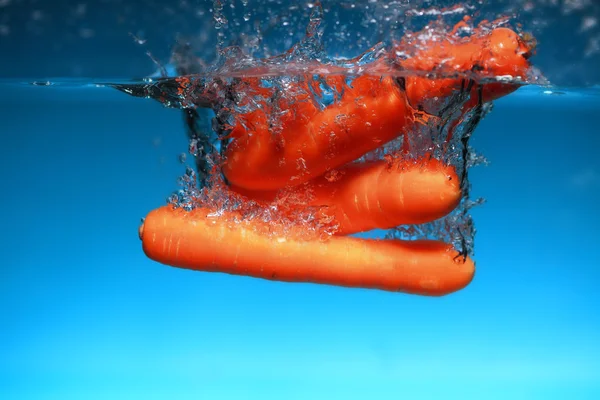 Cenoura no respingo de água sobre azul — Fotografia de Stock