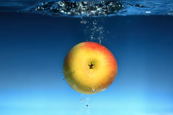 Manzana amarilla en el agua salpica sobre azul —  Fotos de Stock