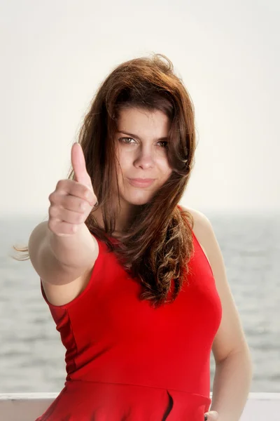 Mladá žena v červených šatech na molo palec nahoru — Stockfoto