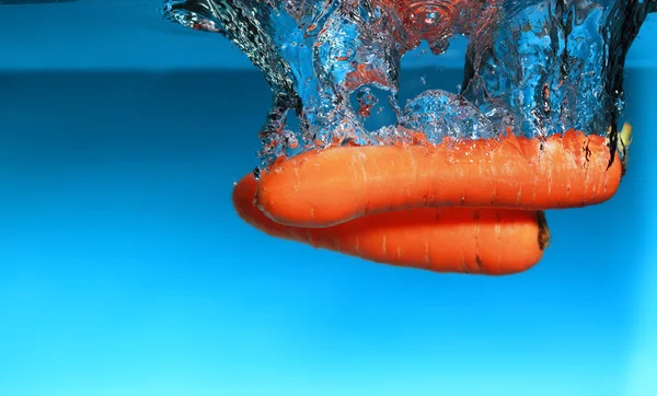 Carota nell'acqua spruzzata sopra il blu — Foto Stock