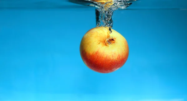 Manzana amarilla en el agua salpica sobre azul —  Fotos de Stock