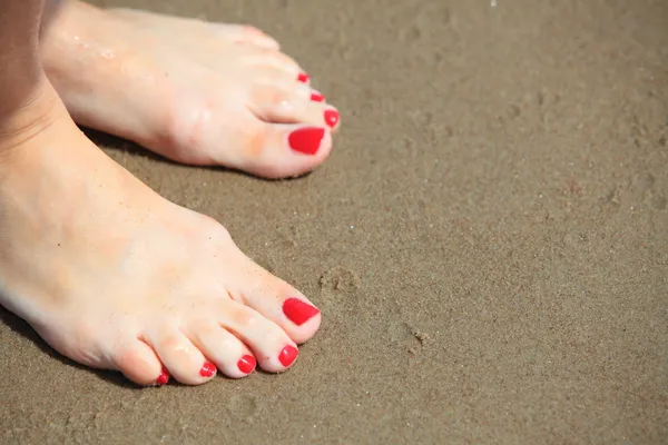 Woman feet with red pedicure relaxing on sand — Stock Photo, Image