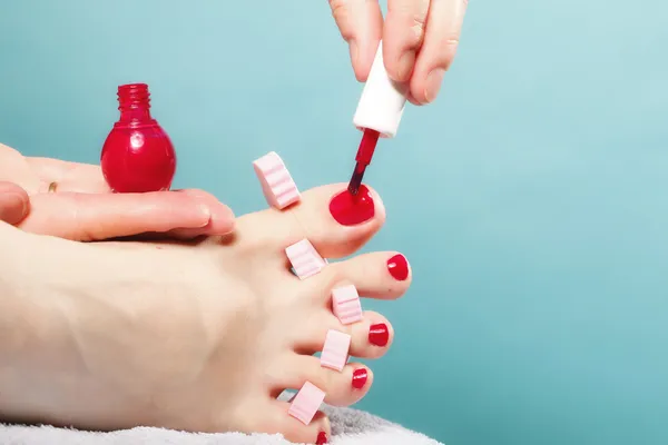 Pedicure del piede applicando unghie rosse su blu — Foto Stock