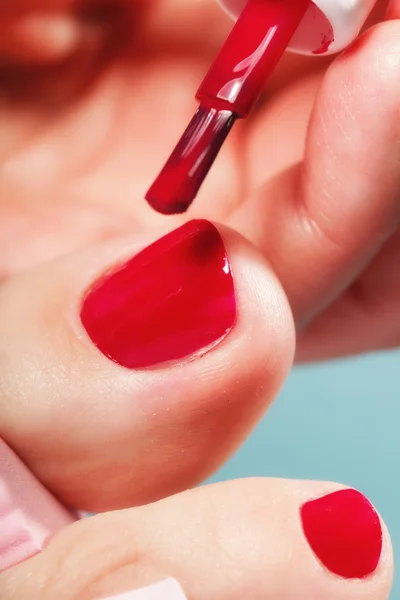 Pedicure del piede applicando unghie rosse su blu — Foto Stock