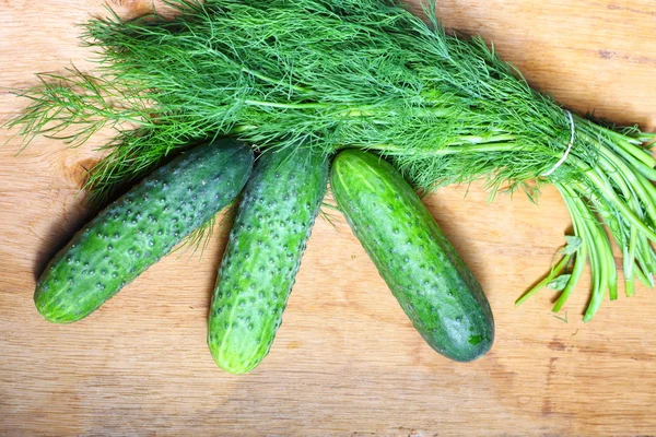 Manojo de eneldo fresco y pepinos en la mesa de madera — Foto de Stock