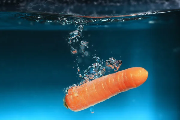 Carota nell'acqua spruzzata sopra il blu — Foto Stock