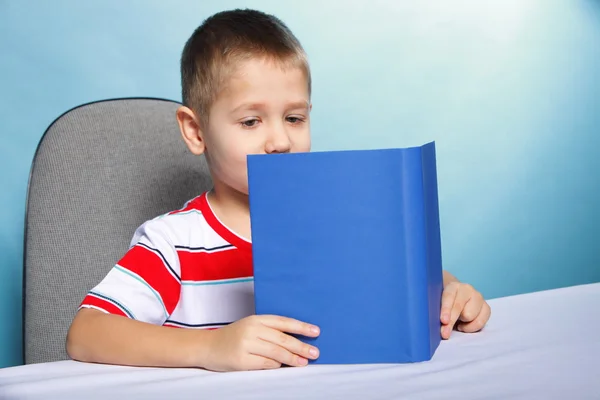 Criança menino criança lendo um livro sobre azul — Fotografia de Stock