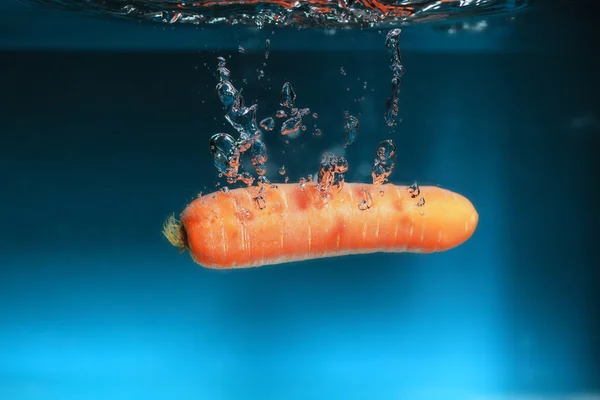 Carota nell'acqua spruzzata sopra il blu — Foto Stock