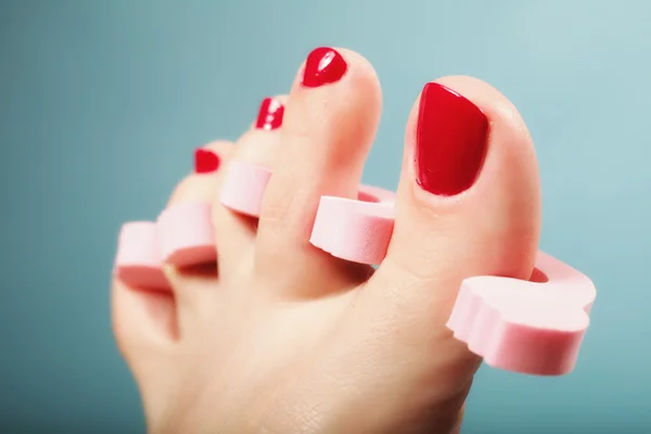 Pedicure del piede applicando unghie rosse su blu — Foto Stock