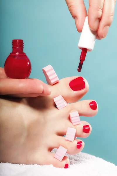 Pedicura del pie aplicando uñas de los pies rojas sobre azul —  Fotos de Stock