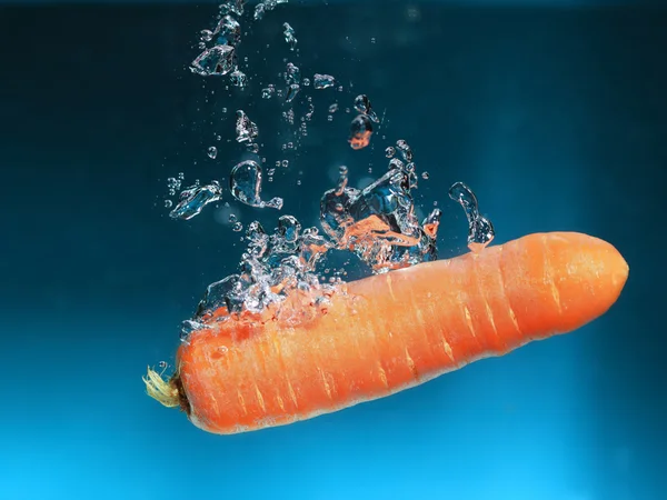 Zanahoria en el agua salpica sobre azul — Foto de Stock