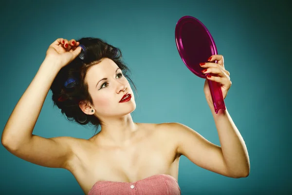 Girl in curlers styling hair looking in mirror — Stock Photo, Image