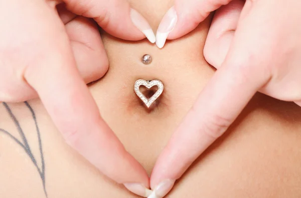 Manos símbolo del corazón alrededor del ombligo piercing — Foto de Stock