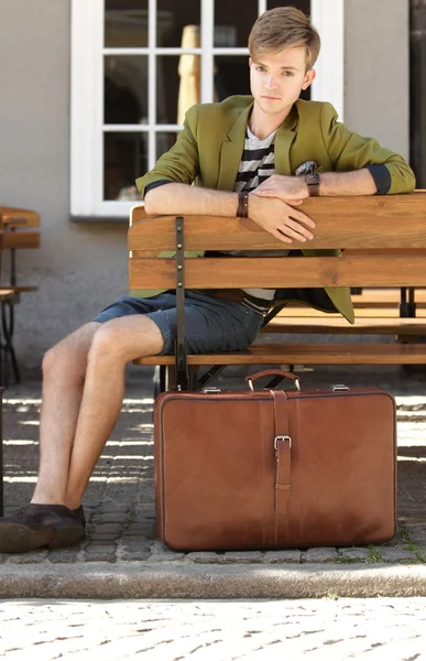 Junger schöner Mann mit Koffer wartet auf Bank — Stockfoto