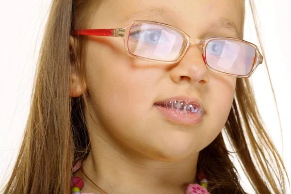 Close up little girl in glasses doing fun saliva bubbles — Stock Photo, Image